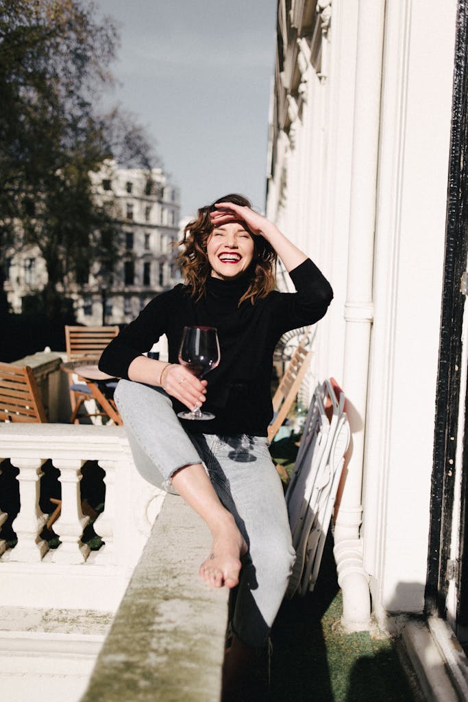 Happy woman with red wine on balcony fence